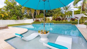 A swimming pool with lounge chairs and a tiki umbrella.