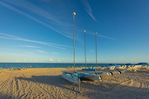 Relax on the beach with sun loungers and umbrellas, surrounded by sailboats and a scenic ocean view.