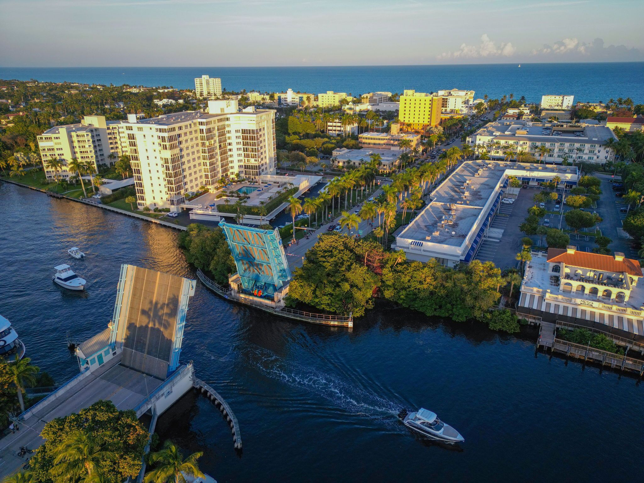 An aerial view of a coastal city with a marina, including a bridge, buildings, and boats.
