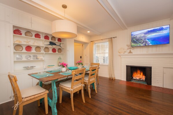 A dining area with a wooden table and chairs, a white fireplace, and a TV mounted on the wall.