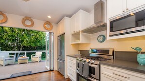 A modern kitchen with white cabinets, stainless steel appliances, and a view of a deck with outdoor furniture. - Pool/Hot Tub/Pet Friendly/Walk To Beach (La Jolla)