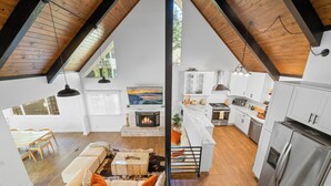 A modern loft with a high ceiling, a fireplace, a dining area, and a kitchen with stainless steel appliances.