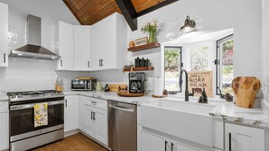A modern kitchen with white cabinets, stainless steel appliances, and a wooden floor.