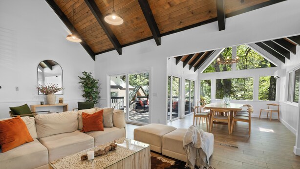 A spacious living room with a high ceiling, a large window, and a dining area with wooden furniture.