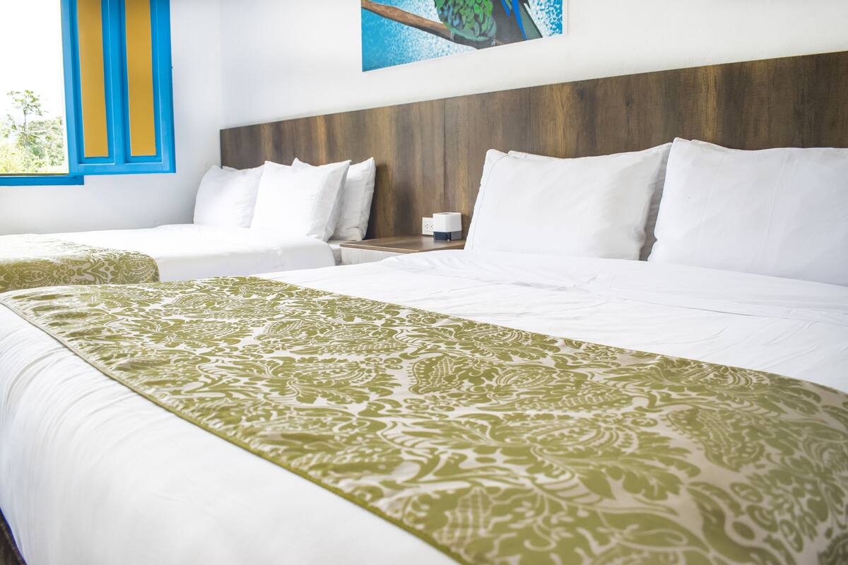 A hotel room with two beds, a wooden headboard, and a window with blue and yellow trim.