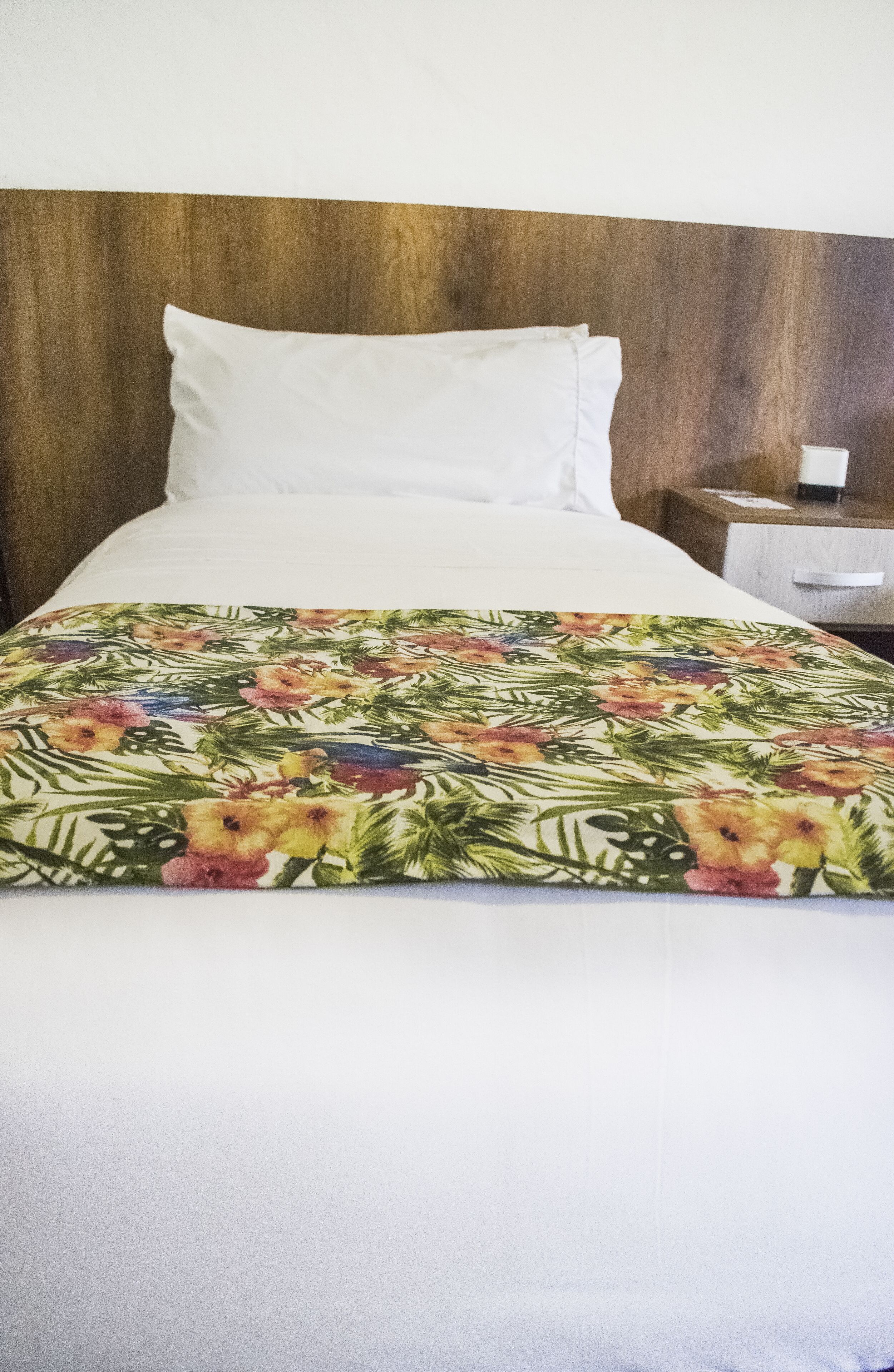 Una cama con un edredón estampado con motivos florales, un cabecero de madera y una almohada blanca.