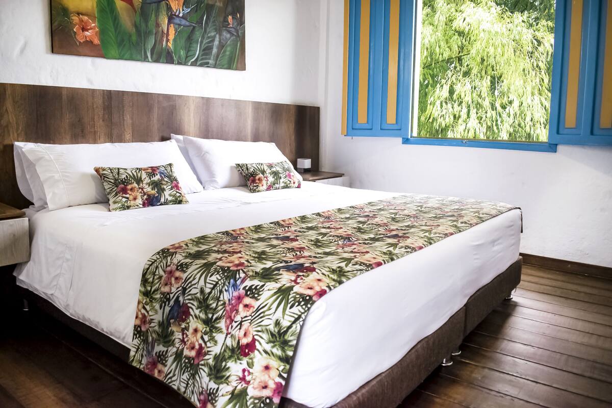 A neatly made bed with a floral bedspread, a wooden headboard, and a nightstand with a lamp.