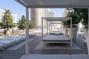 A rooftop terrace with a white canopy, lounge chairs, and a view of high-rise buildings.