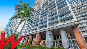 Un hotel de altura con múltiples balcones, un llamativo logo 'W' y una palmera en primer plano.