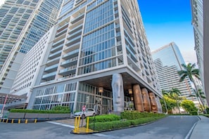 A modern high-rise building with a glass facade, multiple balconies, and a central entrance with a large pillar.