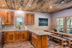 A rustic kitchen with wooden cabinets, a welcome sign, and a large island with benches.
