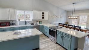 A modern kitchen with white cabinets, a large island, and a dining area with chairs. - Spacious & Secluded Mountain Retreat by Bryce Resort: Ski, Mtn Bike, Game room (Basye)