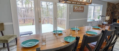 Un comedor con una mesa de madera dispuesta para cuatro personas, sillas negras y vistas al jardín trasero a través de puertas de vidrio.