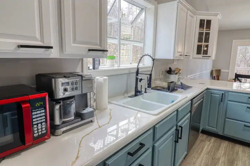 A modern kitchen with white cabinets, a double sink, a red microwave, and a coffee maker.
