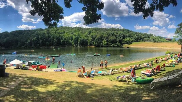 A lakeside setting with boats, a grassy area with sun loungers, and a forested hill in the background. - Spacious & Secluded Mountain Retreat by Bryce Resort: Ski, Mtn Bike, Game room (Basye)