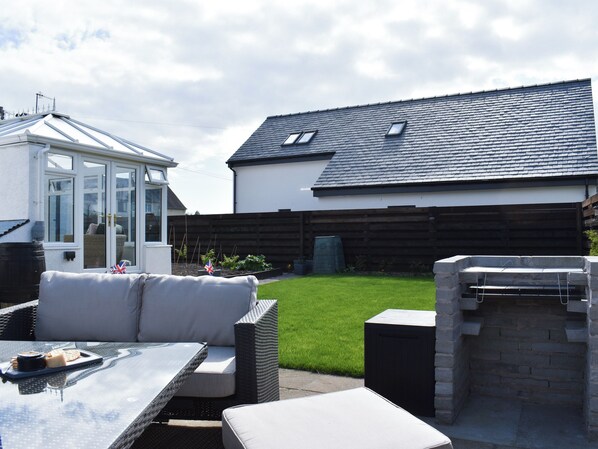 A patio with outdoor furniture, a conservatory, a garden, and a brick oven.