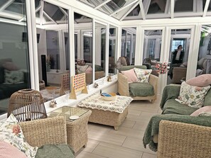 A conservatory with wicker furniture, a table with a lace tablecloth, and a birdcage.