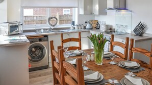 Una cocina moderna con lavadora integrada, un comedor con sillas de madera y vista a un muro de ladrillo.