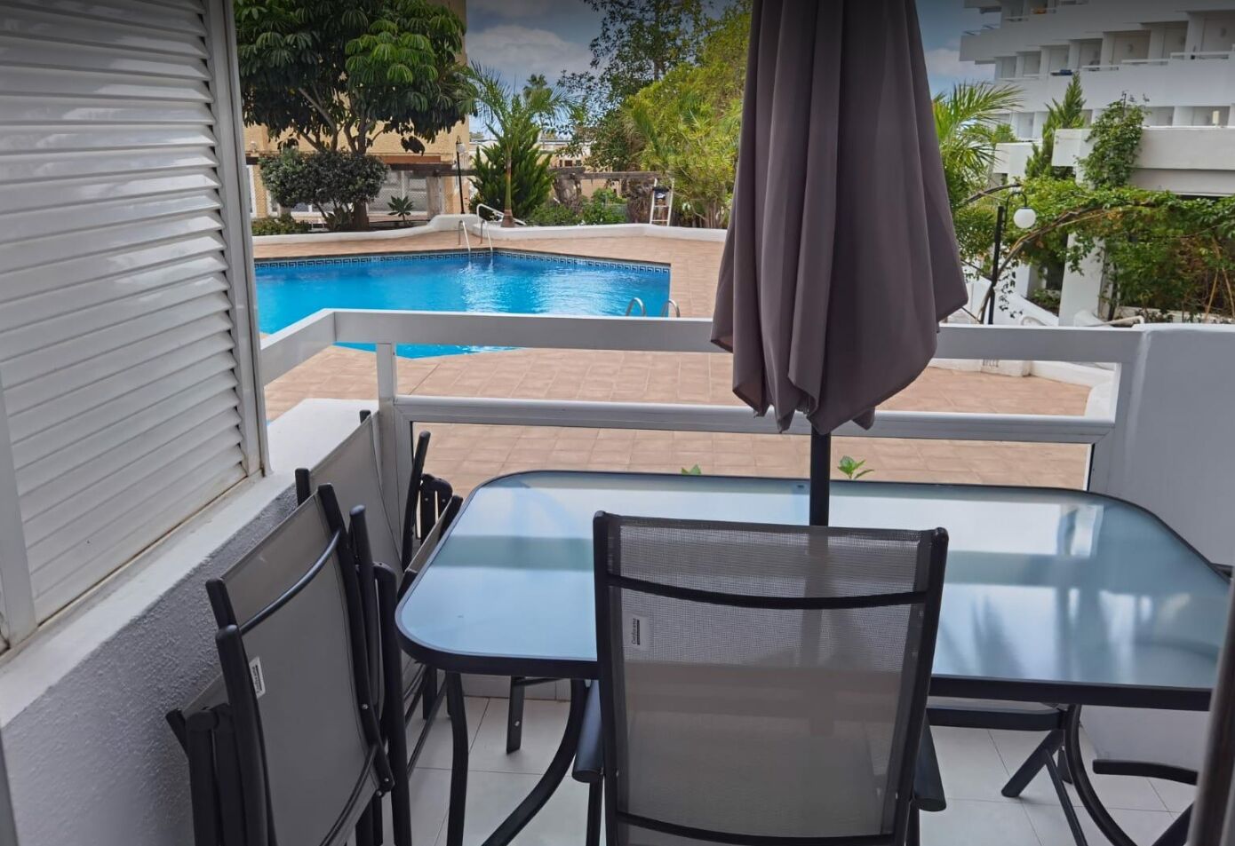 A balcony with a pool view, a table, chairs, and an umbrella.