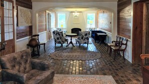 A spacious room with a brick floor, a chandelier, and a fireplace. There are several chairs and a sofa arranged around a table. - Marguerite Bed and Breakfast (St. Gabriel)