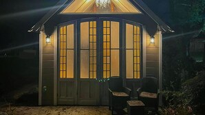 A gazebo-style structure with a triangular roof and a chandelier. It features a set of double doors with illuminated panels and two wall-mounted lanterns. - Marguerite Bed and Breakfast (St. Gabriel)