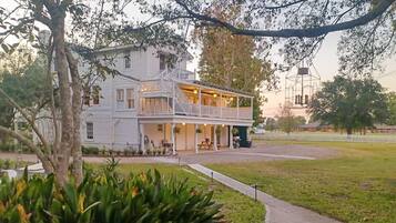 A two-story white building with a balcony, a covered porch, and a lawn in front.