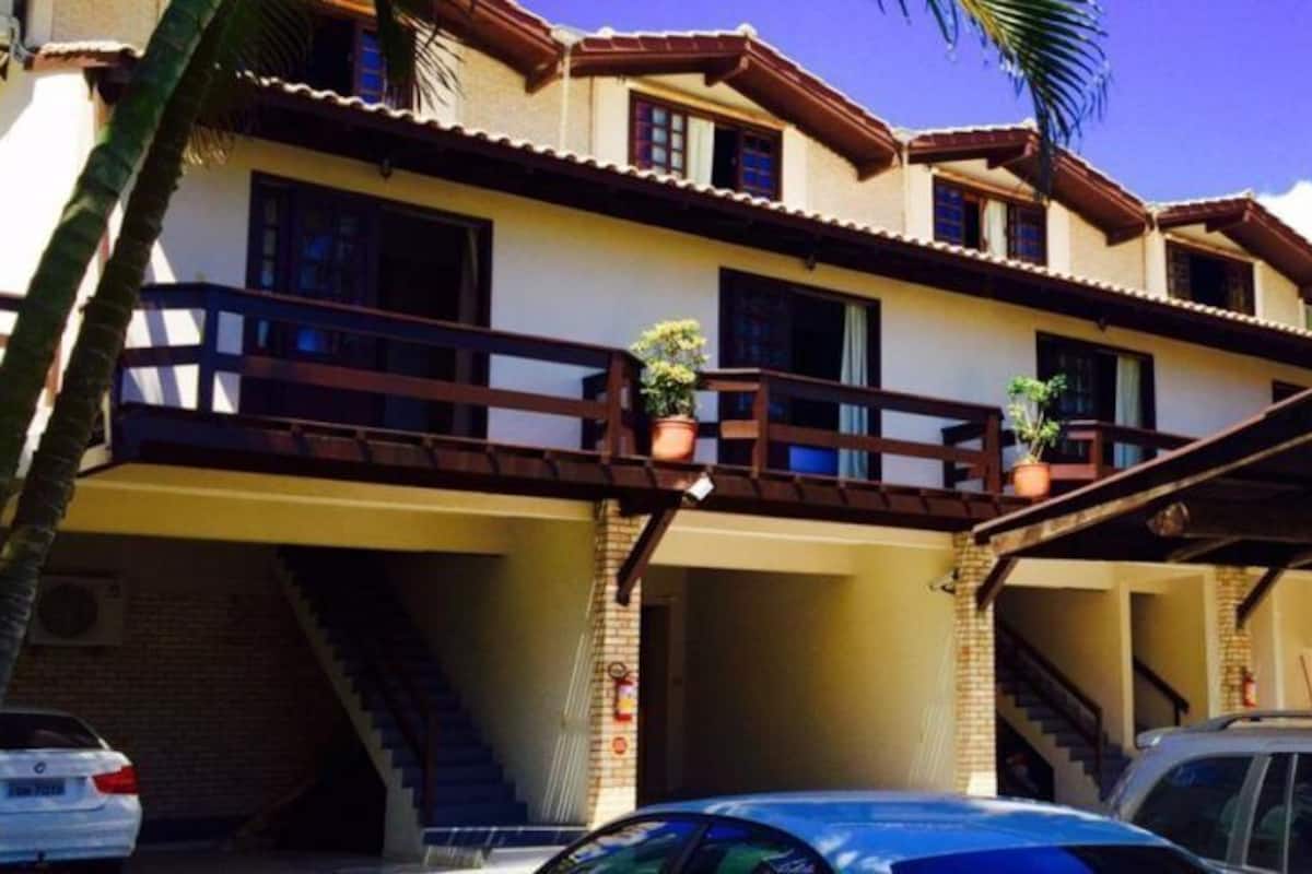 A two-story building with a balcony, a covered parking area, and a staircase leading to the entrance.