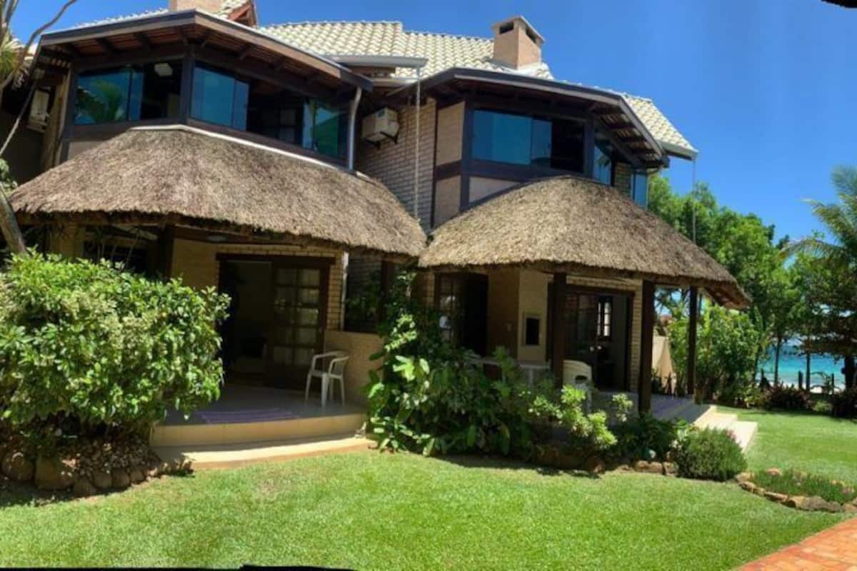 A two-story house with a thatched roof porch, a well-maintained lawn, and a view of the ocean.