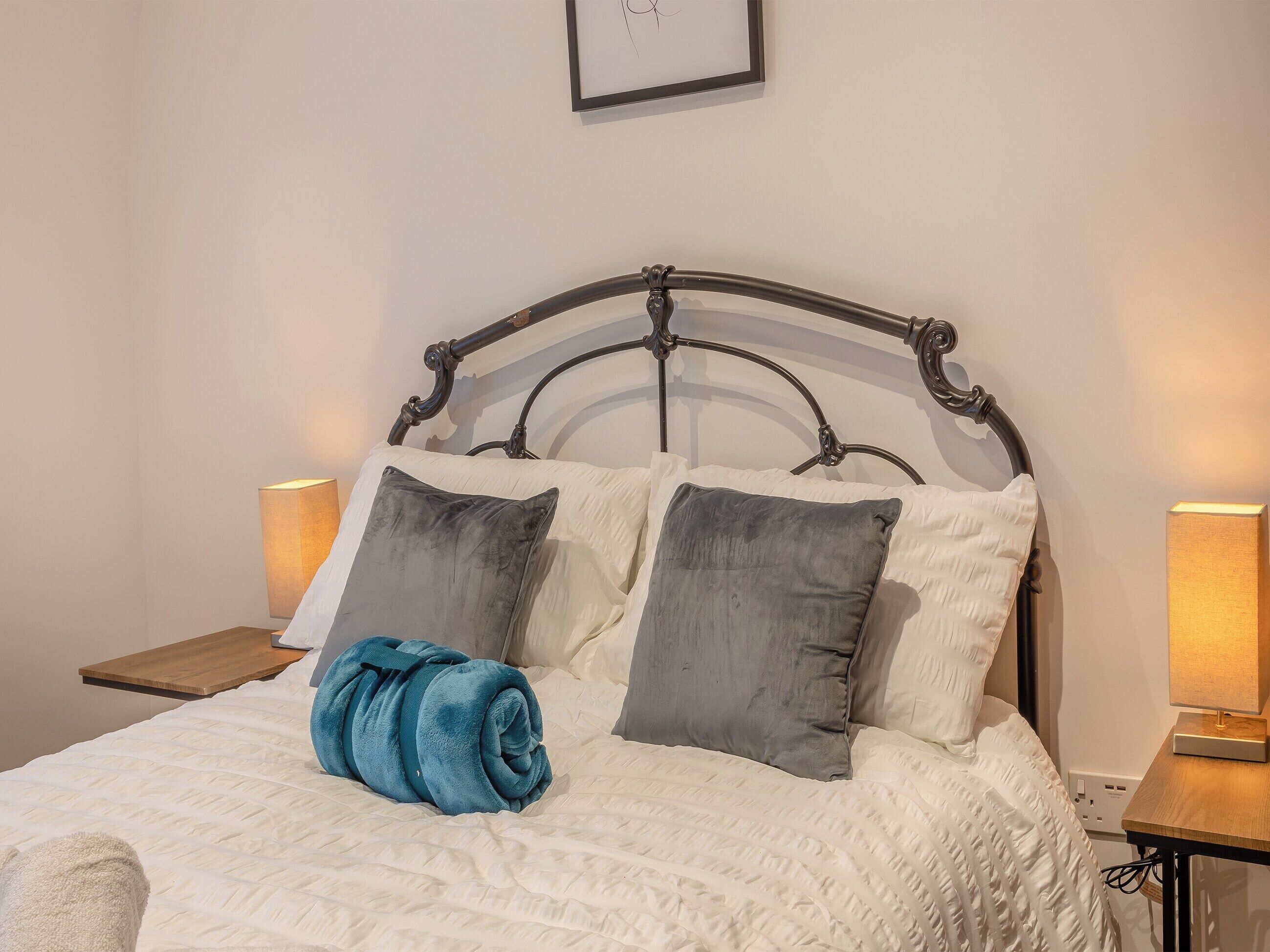 Een net opgemaakt bed met een opgerolde handdoek, twee kussens en een hoofdeinde.