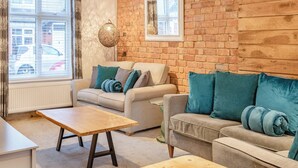 Ein gemütliches Wohnzimmer mit einer Ziegelwand, zwei Sofas mit Türkis-Kissen, einem Holztisch und einer Hängeleuchte.