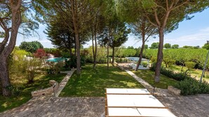 A garden patio with a table set for a meal, surrounded by trees and a swimming pool in the background. - 2920 Villa Oasis by Perle di Puglia (Mottola)