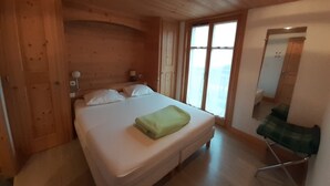 Ein Zimmer mit Holzboden, einem Bett, einem Spiegel und einem Fenster.