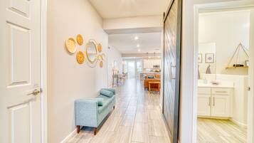 A hallway with a light-colored floor, a blue sofa, and a dining area in the background.