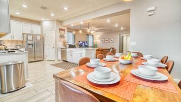 A modern kitchen with white cabinets, a stainless steel refrigerator, and a dining area with a wooden table set for a meal.