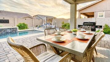 A poolside dining area with wicker chairs and a table set for four, overlooking a swimming pool and a brick wall.