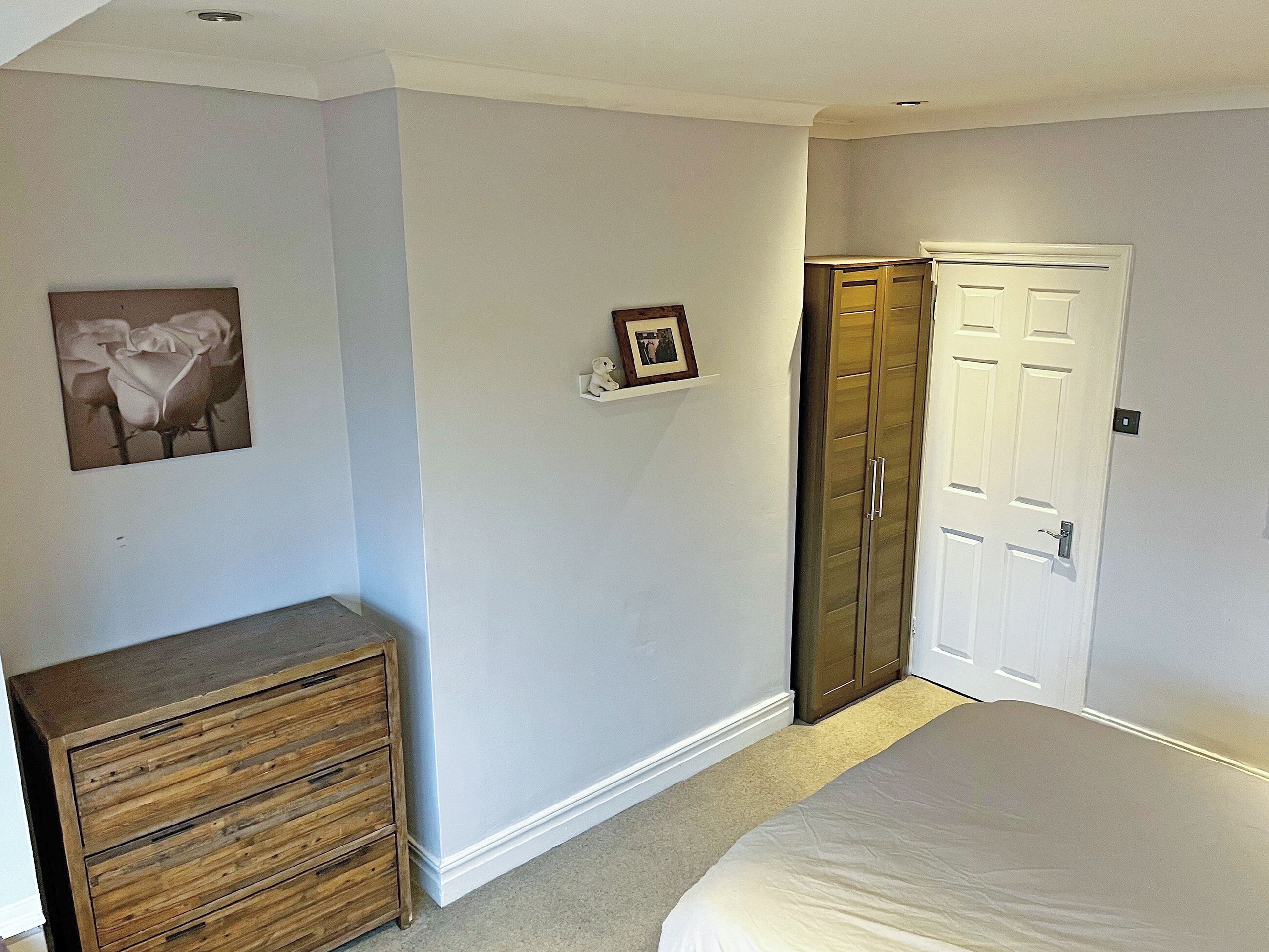 A bedroom with a bed, a dresser, a wardrobe, and a framed picture on the wall.