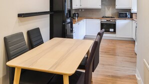A compact kitchen with white cabinets, a black refrigerator, a microwave, and a stove. There is a wooden dining table with four chairs. - 3 bedroom accommodation in Tynemouth (Tynemouth)