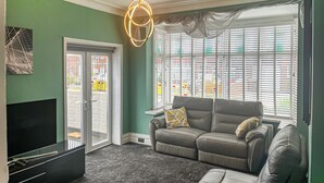 A living room with a sofa, a TV, and a large window with blinds. - 3 bedroom accommodation in Tynemouth (Tynemouth)