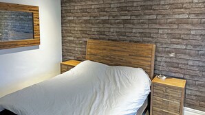 A bedroom with a wooden headboard, a bed with white bedding, a nightstand, and a wall-mounted mirror. - 3 bedroom accommodation in Tynemouth (Tynemouth)