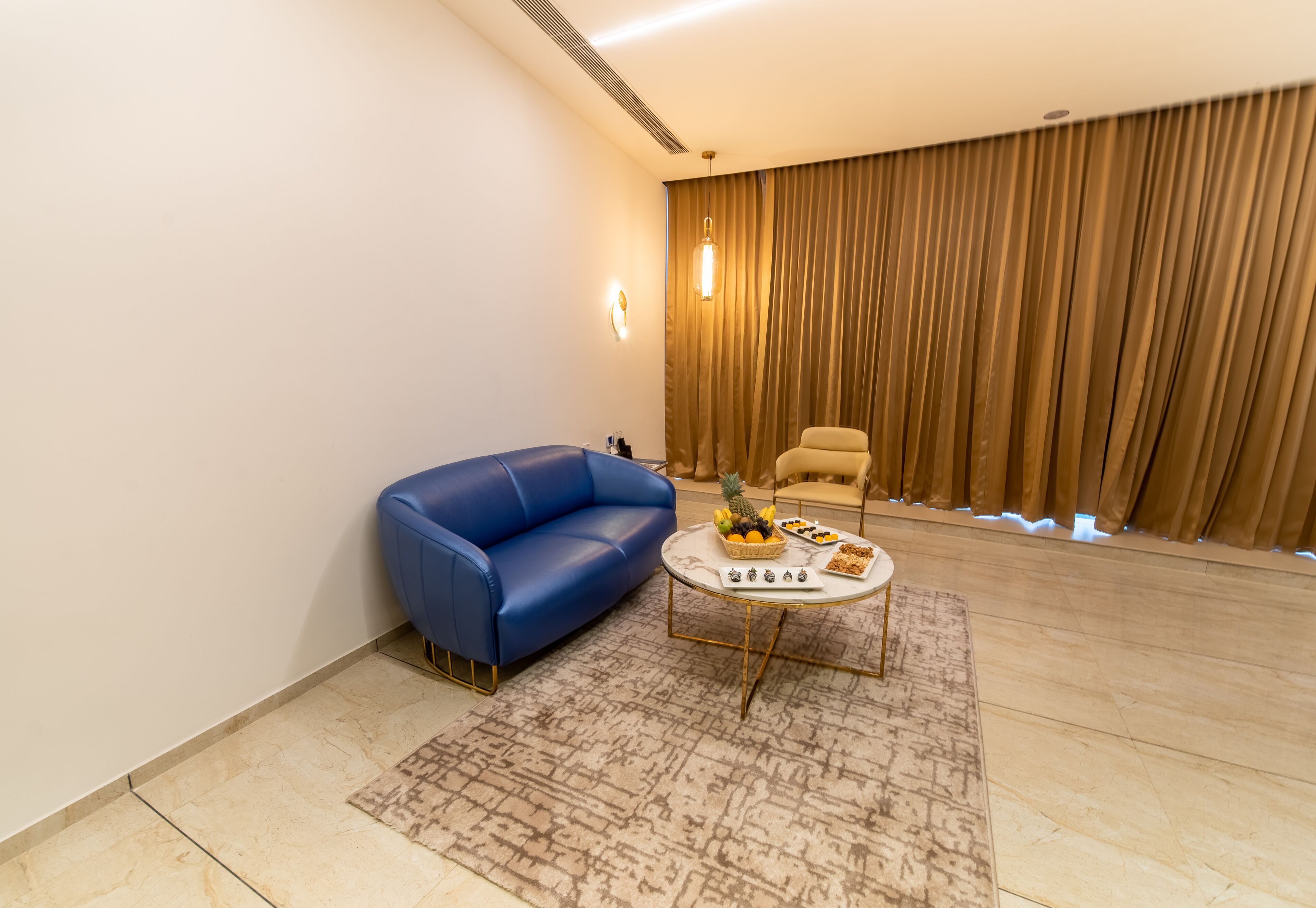 A modern living room with a blue sofa, a coffee table with fruit, and a beige armchair.