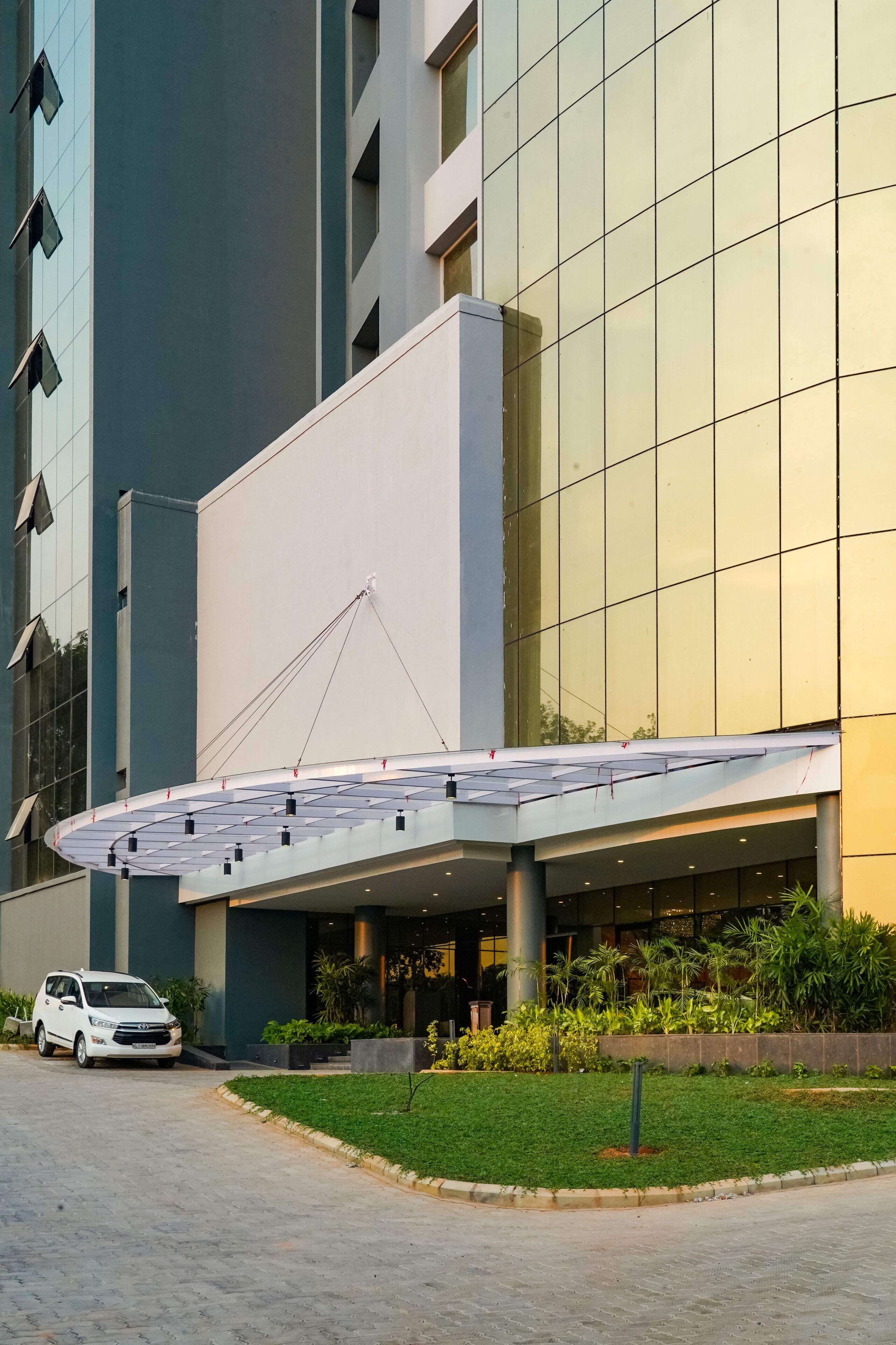 A modern building with a glass facade, a covered entrance, and a parking area with a white car.