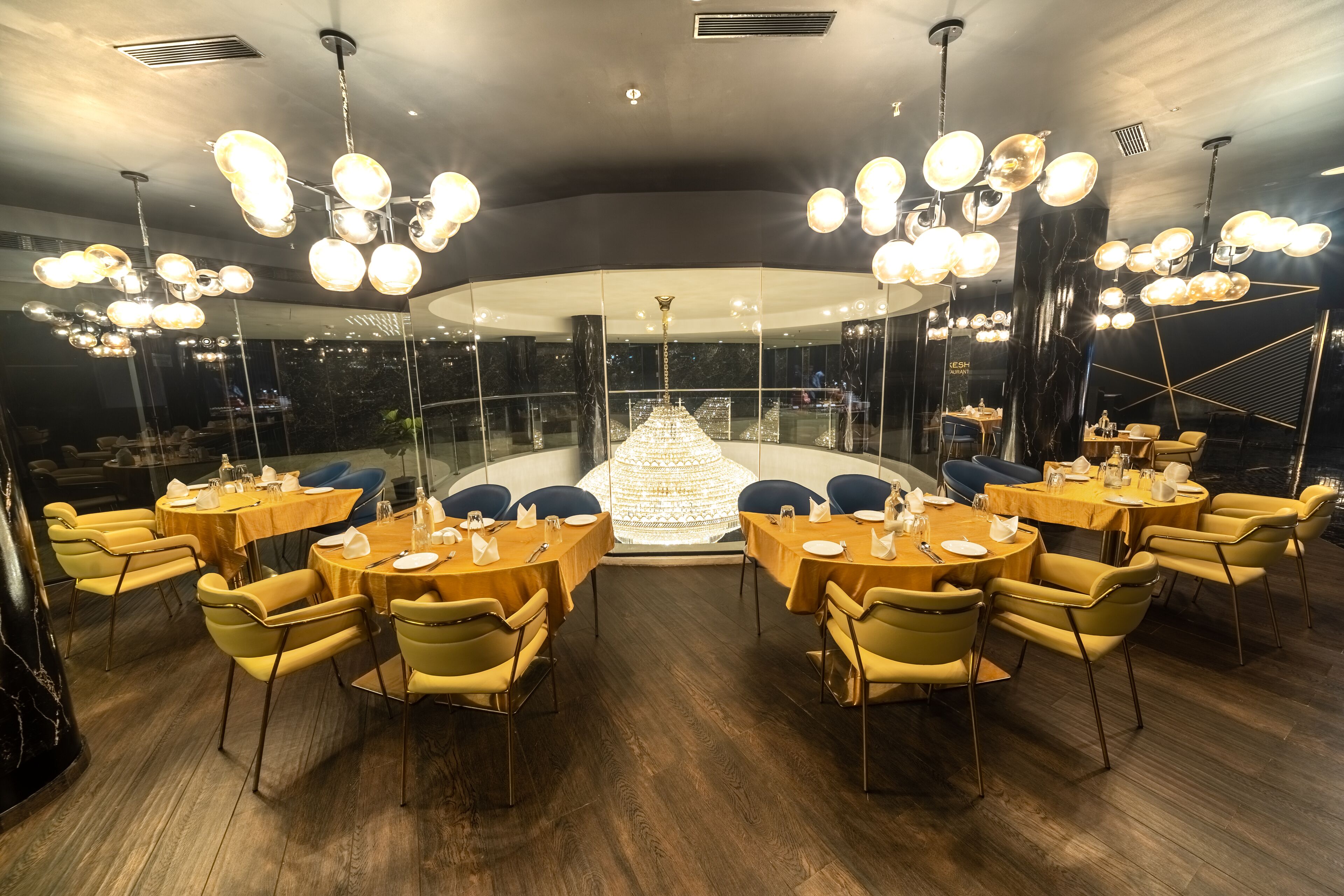 A restaurant with round tables and yellow chairs, a chandelier, and a view of the city.