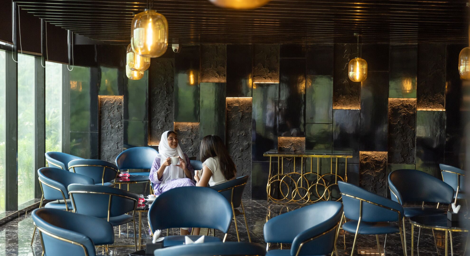 A modern interior with blue chairs, a marble floor, and a stone wall with embedded lights.