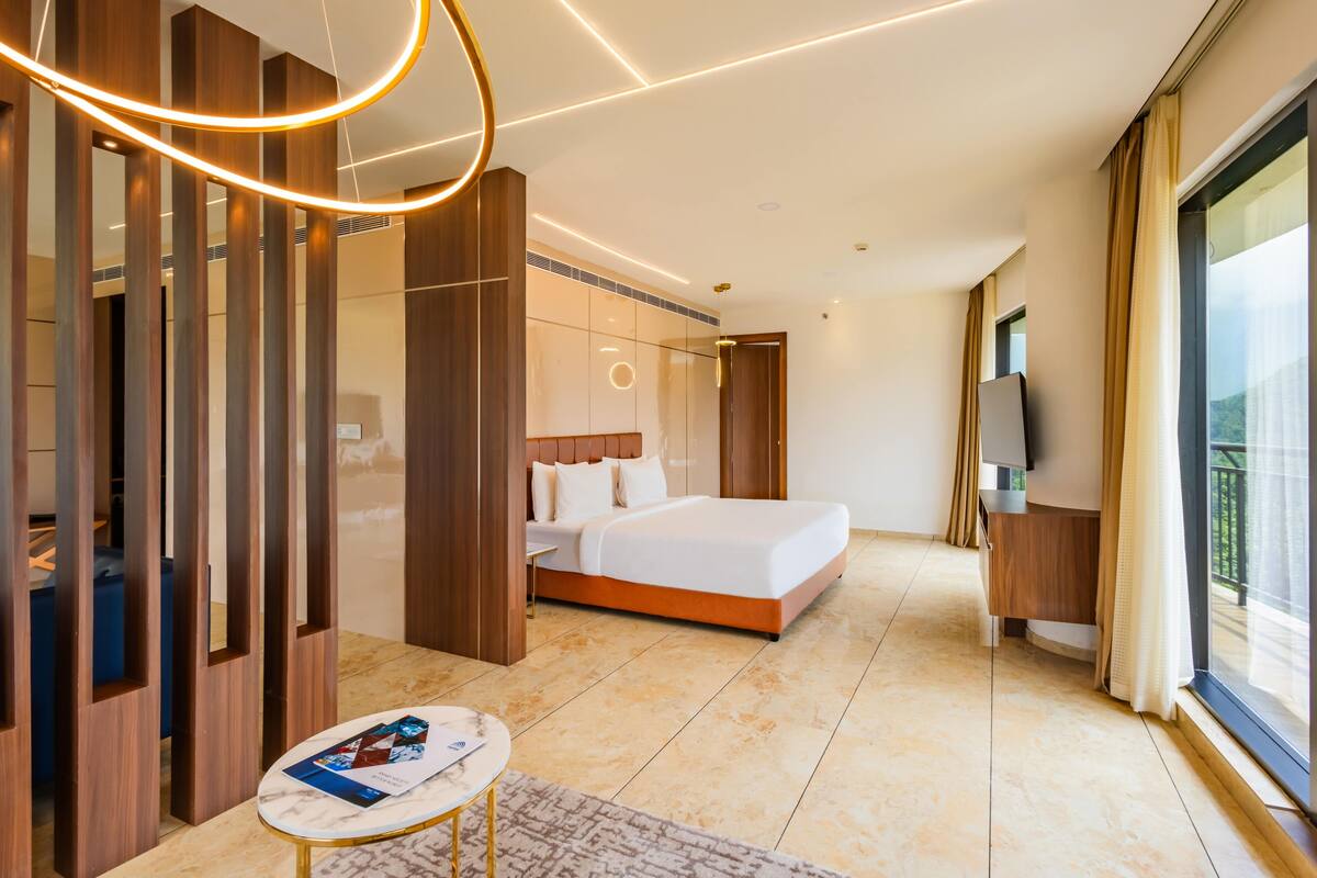 Una habitación de hotel moderna con una cama grande, televisión y balcón con cortinas.