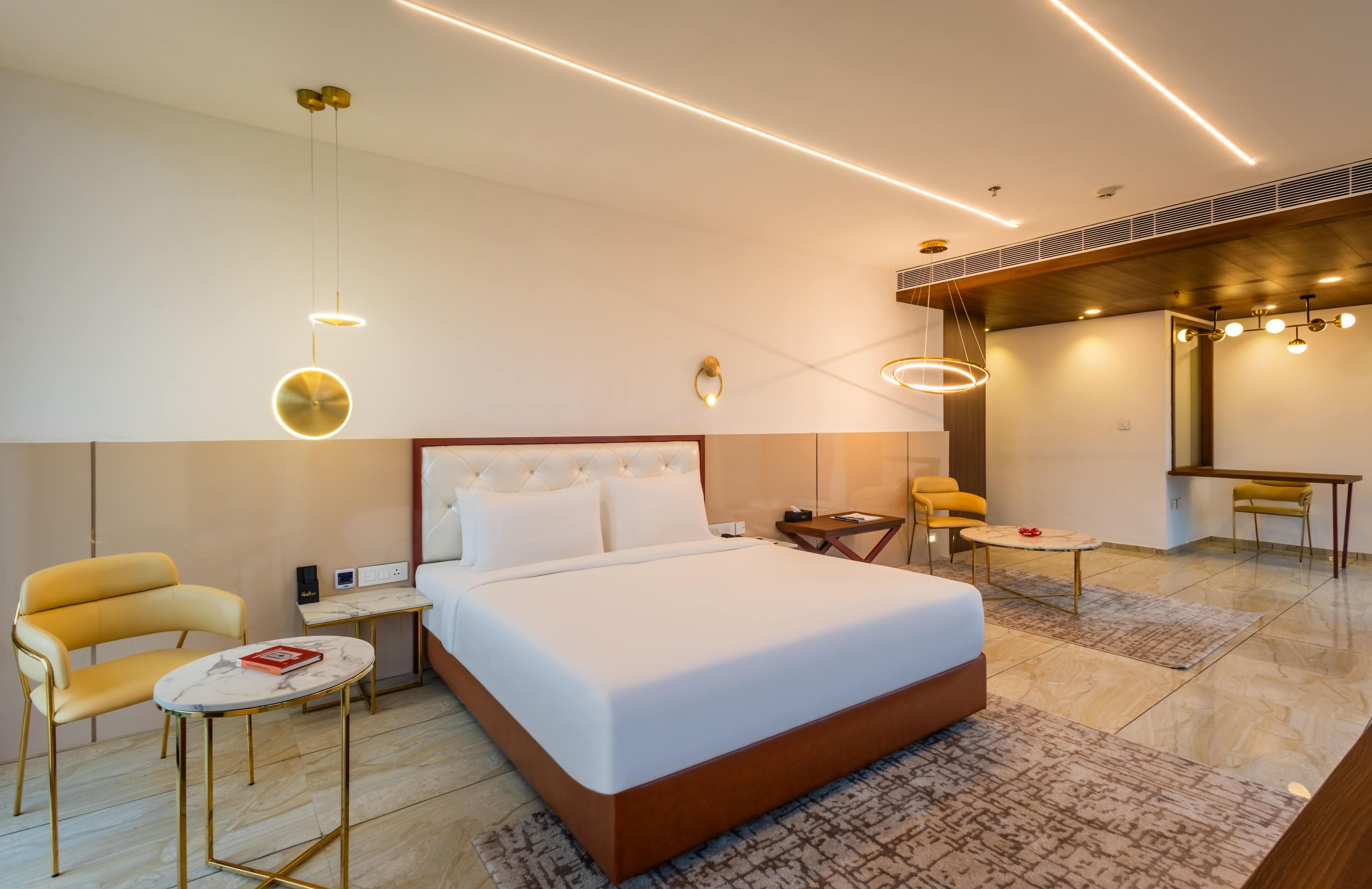 A modern hotel room with a large bed, a sitting area with a sofa and chairs, a small table, and a desk.