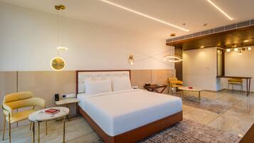 A modern hotel room with a large bed, a sitting area with a sofa and chairs, a small table, and a desk.