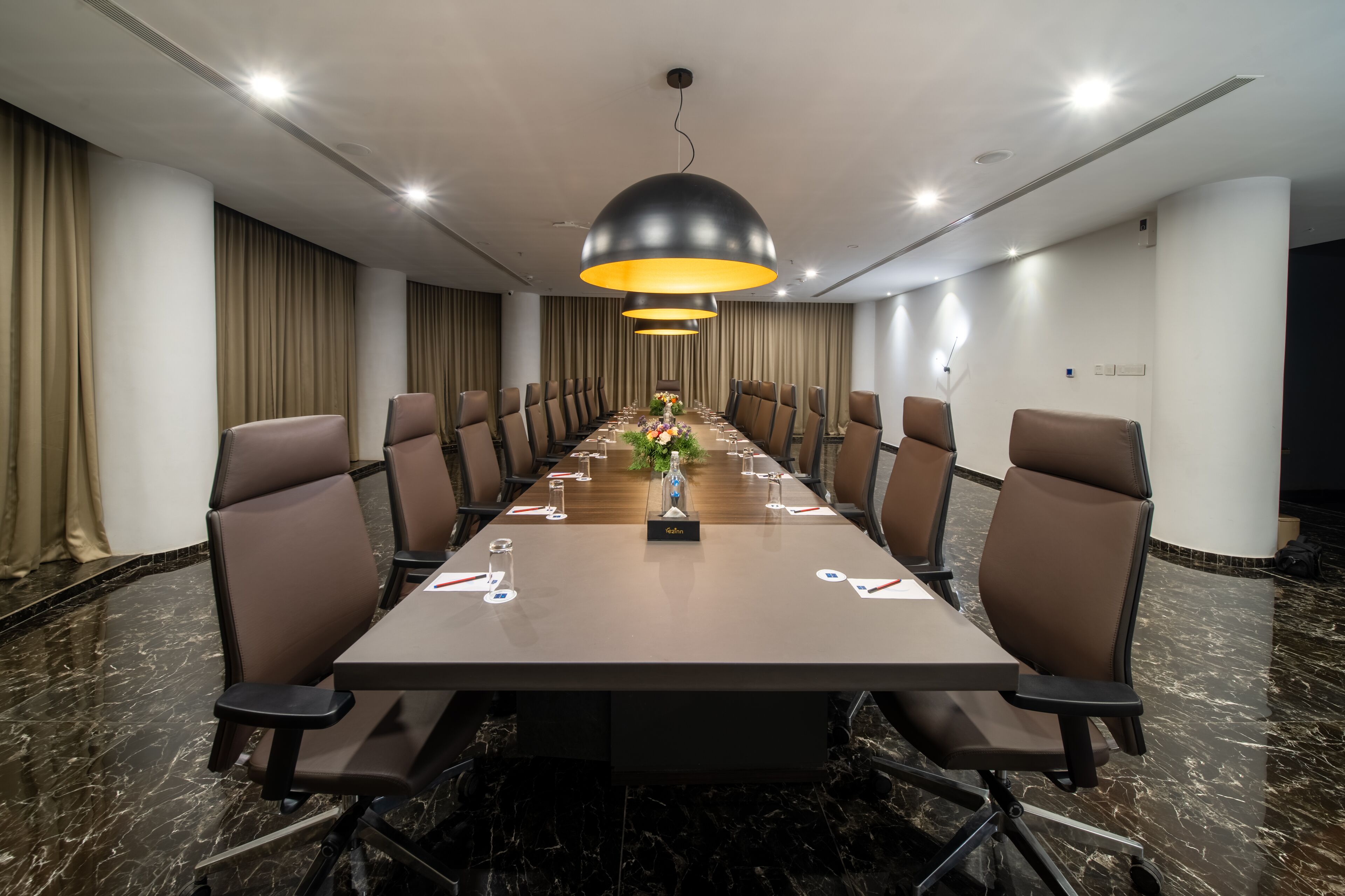 Un salón de conferencias con una larga mesa, sillas marrones y una lámpara de araña central.