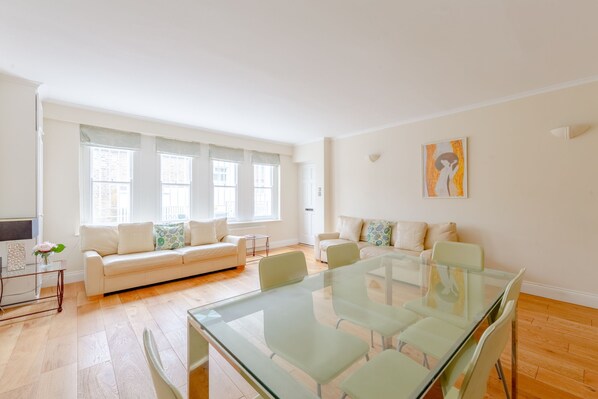 A spacious living room with a glass dining table, two sofas, and large windows.