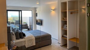 A modern bedroom with a bed, a TV, a glass door leading to a balcony, and built-in shelving. - Luxury Suite with a queen's double bed and private jacuzzi. (SKIATHOS)