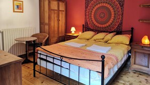 A bedroom with a bed, wooden wardrobe, a chair, a table, a tapestry, and a heater. - Beautiful River-front Villa with Natural Pool & Aircon (Sorède)